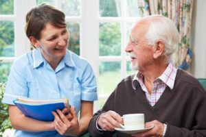 A friendly caregiver assisting an older adult with walking down a well-lit hallway in a residential care setting.